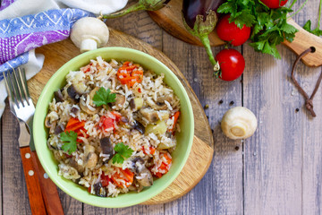 Vegetarian menu, healthy diet food. Rice with vegetables, mushrooms and eggplants in a bowl on a wooden table. Top view on a flat lay.
