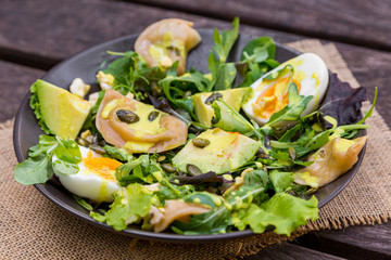 Salad with avocado, dumplings, eggs, pumpkin seeds, arugula and other greens on wooden table in the village. Healthy food concept.