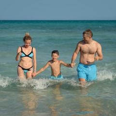 Mother, father and son spending time on sea beach on summer vacations. They are coming out of water.