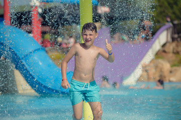Cute European boy in blue swimming shorts having fun in aqua park he is jumping in pool making lots...