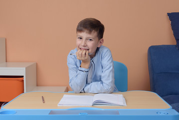 Naklejka premium Cheerful Caucasian schoolboy in uniform doing task at classroom. First time to school. Back to school.