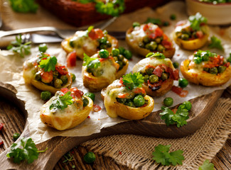 Baked potatoes stuffed with green peas, cheese and bacon sprinkled with green parsley, close up view. The perfect appetizer
