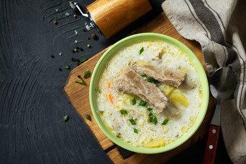 Hot homemade soup with meat ribs and vegetables on a stone countertop. Top view on a flat background lay. Copy space.
