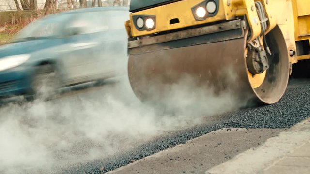 Compactor driving over the hot and steaming asphalt on the road at a construction site