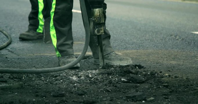 Slow motion of a construction worker using a jack-hammer to break the road apart for street maintenance
