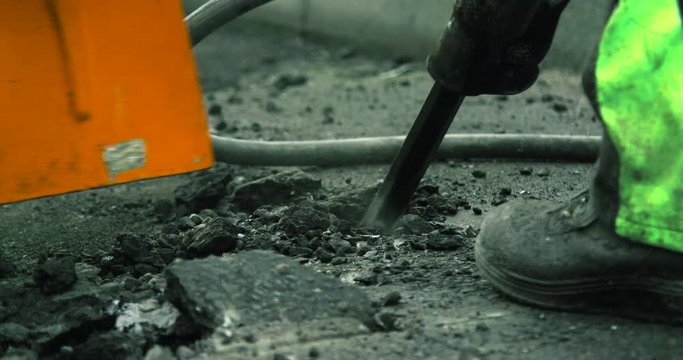 Slow motion of construction worker using a jackhammer destroying the asphalt of a street