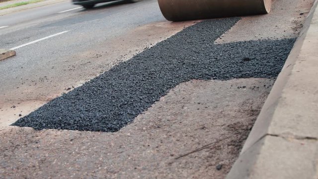 Close up view of freshly patched up road with hot asphalt driven over by compactor