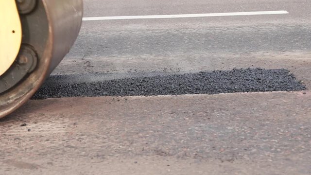 Slow motion of compactor vehicle driving over new hot and steaming asphalt