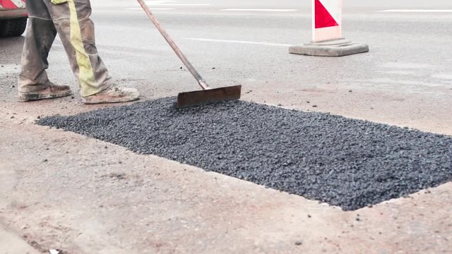 Construction worker is distributing new poured asphalt on the road and prepares it for being compressed
