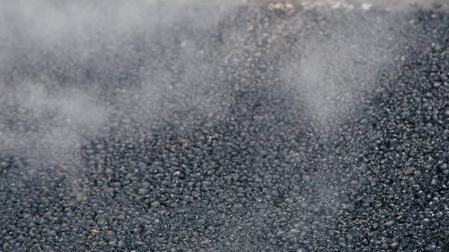 Close up of hot and steaming freshly poured asphalt being compressed by drum machine wagon