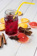 Glass cup with a red drink on a light background, next to slices of dried citrus fruits, cinnamon and anise.