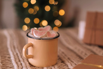 Homemade cocoa with marshmallows in an iron mug on a background of blurry lights.