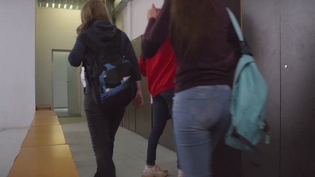 Team of young female soccer players with backpacks walking into locker room and changing clothes while preparing for training