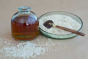 sesame oil in blue transparent bottle with sesame seeds in blue transparent plate with bamboo spoon on light background