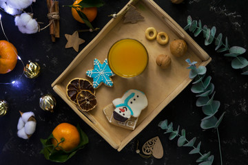 Christmas cookies in the shape of a house, a snowman and stars lie in the gap with fresh orange juice in a glass of farm-style drink. Around nuts, cinnamon, decor. Black background.