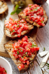 Bruschetta with tomatoes, fresh basil and olive oil on a wooden board, close up, top view. Traditional mediterranean cuisine
