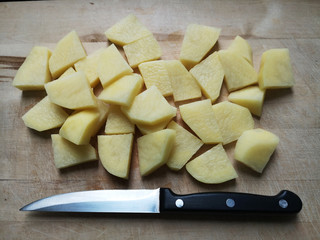 Potato cut into slices or pieces on cutting board along with cook's knife. Process of traditional everyday food cooking. Flat lay or top view photo.