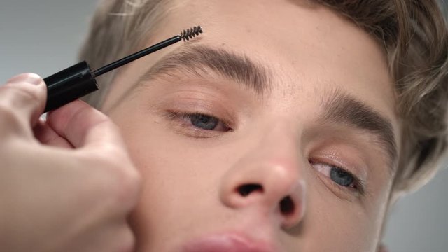 Macro of upper face of young man with blue eyes and eyebrow mascara brush coloring and shaping his eyebrows
