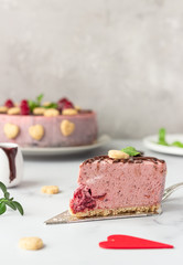 Sliced no bake raspberry cheesecake (cream mousse dessert) decorated with chocolate glaze, raspberries, heart shape cookies and mint. Valentine’s day concept. Selective focus.