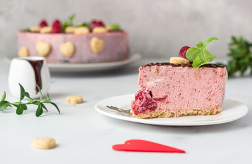 Sliced no bake raspberry cheesecake (cream mousse dessert) decorated with chocolate glaze, raspberries, heart shape cookies and mint. Valentine’s day concept. Selective focus.