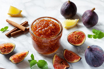 Fresh figs, with a dish of homemade fig jam or preserves with lemon cinnamon sticks and mint on white kitchen marble table background. Healthy breakfast dessert snack recipes and veggie tables concept