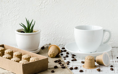 Fototapeta na wymiar Coffee capsules made from wood. Wooden espresso coffee Capsules, white cup of coffe, coffee beans and flower in a pot on whie wooden table. Zero waste and no plastic concept
