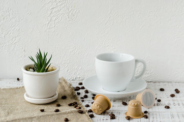 Coffee capsules made from wood. Wooden espresso coffee Capsules, white cup of coffe, coffee beans and flower in a pot on whie wooden table. Zero waste and no plastic concept