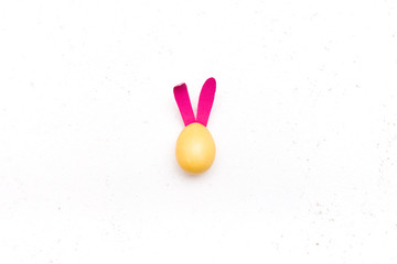 yellow easter egg with pink rabbit ears on a white background, top view, copy space, texture background, central composition
