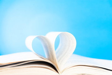 Pages of a book curved into a heart shape on blue background