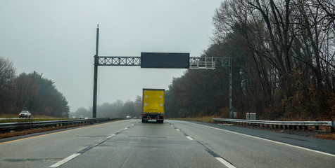 Blank electric digital road sign over a highway with a yellow truck directly underneath it