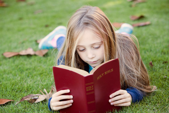 Little Girl Reads Bible Outdoors