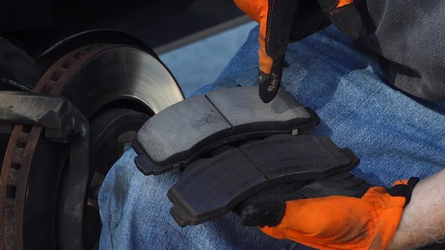Close up of a man's hands showing new and old, dangerously worn out brake pads