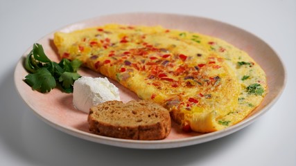 Omelet with cheese, bell pepper, sour cream, brown bread and parsley on a white table