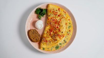 Omelet with cheese, bell pepper, sour cream, brown bread and parsley on a white table