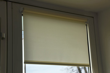 rolled textile blinds on a plastic window in a room, object of protection against sunlight close up.