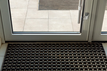 threshold with a rubber foot mat in the front glass door of the office with tiles on the floor...