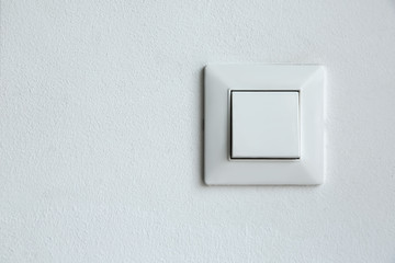 a square shaped white plastic light switch mounted on a white textured wall with a copy space, a...