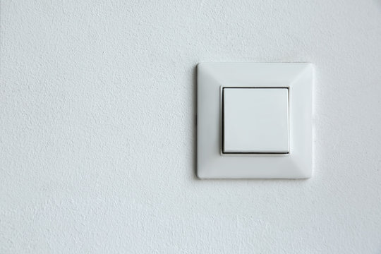 a square shaped white plastic light switch mounted on a white textured wall with a copy space, a conceptual background for interesting ideas.