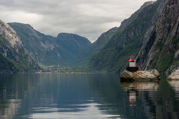 Fototapeta premium Small idyllic lighthouse surrounded by mountains in the majestic Lysefjord in Norway. Seen from the seaside
