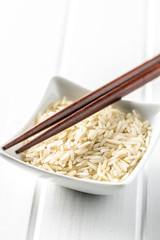 Uncooked indian long rice in bowl and chopsticks.