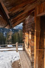 Fototapeta na wymiar Holz dach und Wand er Alm hÜtter im Schnee mit Zaun und Blick auf Wald in der Sonne