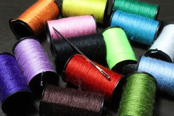 An embroidery needle laying atop a collection of colorful bobbins of thread.Sewing is the craft of...