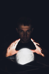 Spiritual session predicting the future. A clairvoyant man holds his hands over a luminous crystal ball.