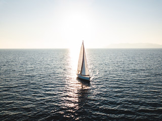 Silhouette of a yacht under sail opposite the reflection of the sun from the water