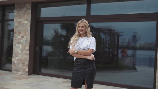 Happy blonde with shirt and leather skirt thoughtfully poses at building