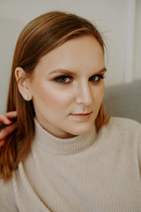 Naklejka premium Portrait of Woman with bright makeup and strict facial features dressed in beige sweater sitting on bed