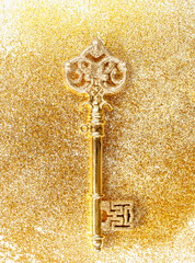 Golden key with sparkles on a background with glitter top view.