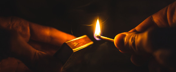 A match lit in the dark in hands with a matchbox - Powered by Adobe