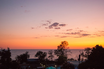 Obraz premium Sunset over the sea - view of a pink sky with purple clouds and contrasting trees. Subtropics, summer, heat, rest, vacation, relaxation, evening, night.