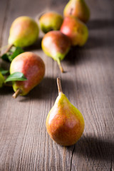Ripe pears with green leaves are scattered on wooden boards. Harvest concept